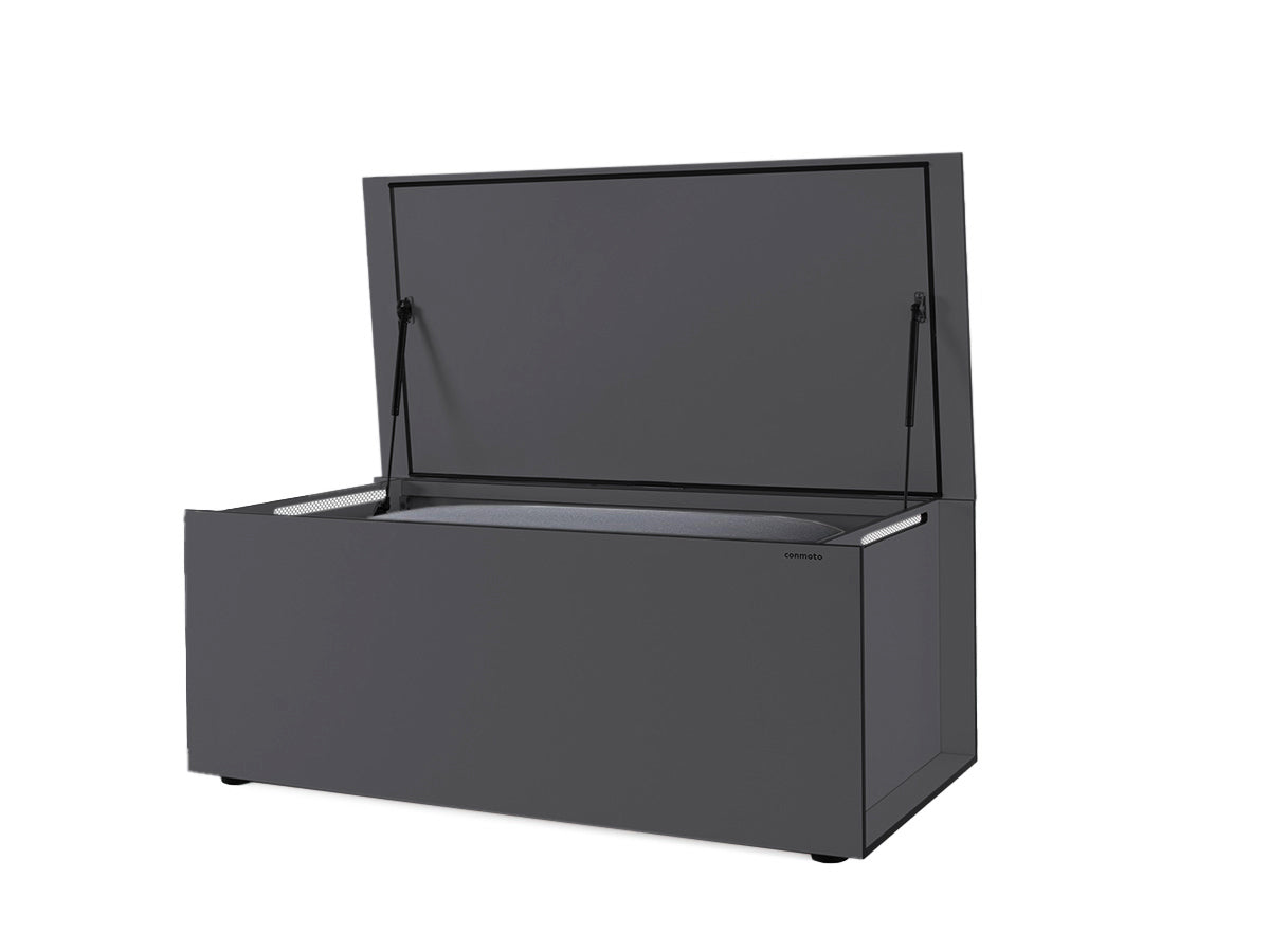 Graue Kissentruhe aus wetterbeständigem HPL-Material mit offenem Deckel. Die klare, rechteckige Form und minimalistisches Design zeichnen das Möbelstück aus. Gasdruckfedern halten den Deckel, integrierte Lüftungsschlitze und eine Gummidichtung am Rand sorgen für Belüftung und Wasserdichtigkeit. Die Truhe sitzt auf verstellbaren Füßen für Stabilität auf unebenem Boden.