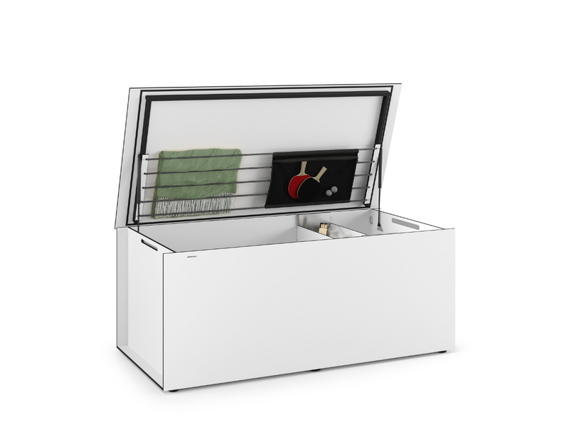 Weiße Kissentruhe von Conmoto mit geöffnetem Deckel, innen ausgestattet mit einem Meshbag. Der Meshbag hat ein Netzdesign, das elastische Streifen zur Befestigung nutzt. Im Meshbag befinden sich ein grüner Stoff und ein schwarzer Beutel mit Tischtennisschlägern und Bällen. Der Innenraum der Truhe ist in Fächer unterteilt und enthält einen Pinsel.