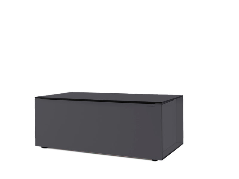 Rechteckige Kissentruhe in dunklem Grau, minimalistisch gestaltet mit glatten Oberflächen und klaren Linien. Die Vorderseite zeigt ein dezentes Logo in der oberen Ecke. Der Deckel ist flach und dezent abgesetzt. Die Truhe steht auf kleinen, runden Füßen.