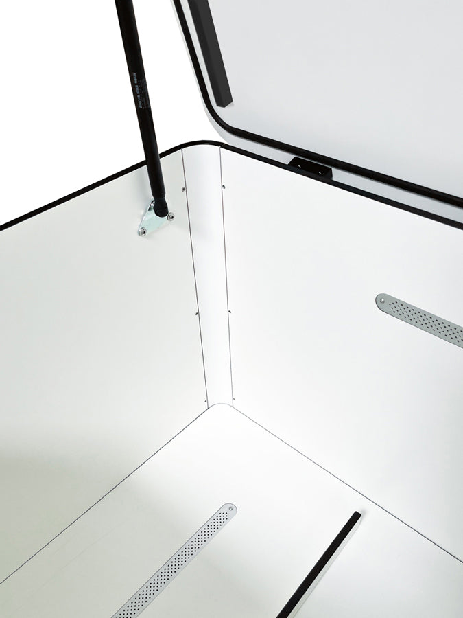 Offene RONDA Kissentruhe in Weiß mit Gasdruckfeder am Deckel, die das Öffnen erleichtert. Die Innenseite zeigt einen glatten, weißen HPL-Korpus mit Belüftungsschlitzen, die eine optimale Luftzirkulation ermöglichen. Der kontrastierende schwarze Rand des Deckels und der Gasdruckfedermechanismus betonen das moderne Design.